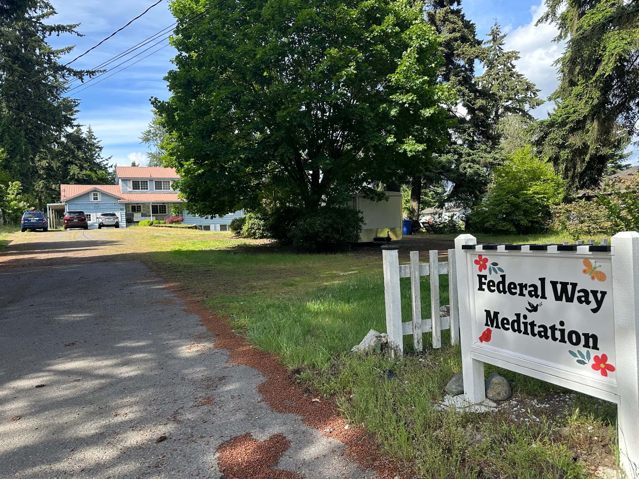 The entrance to Federal Way Meditation — a white Federal Way Meditation sign beside the gravel driveway, with the blue house behind it